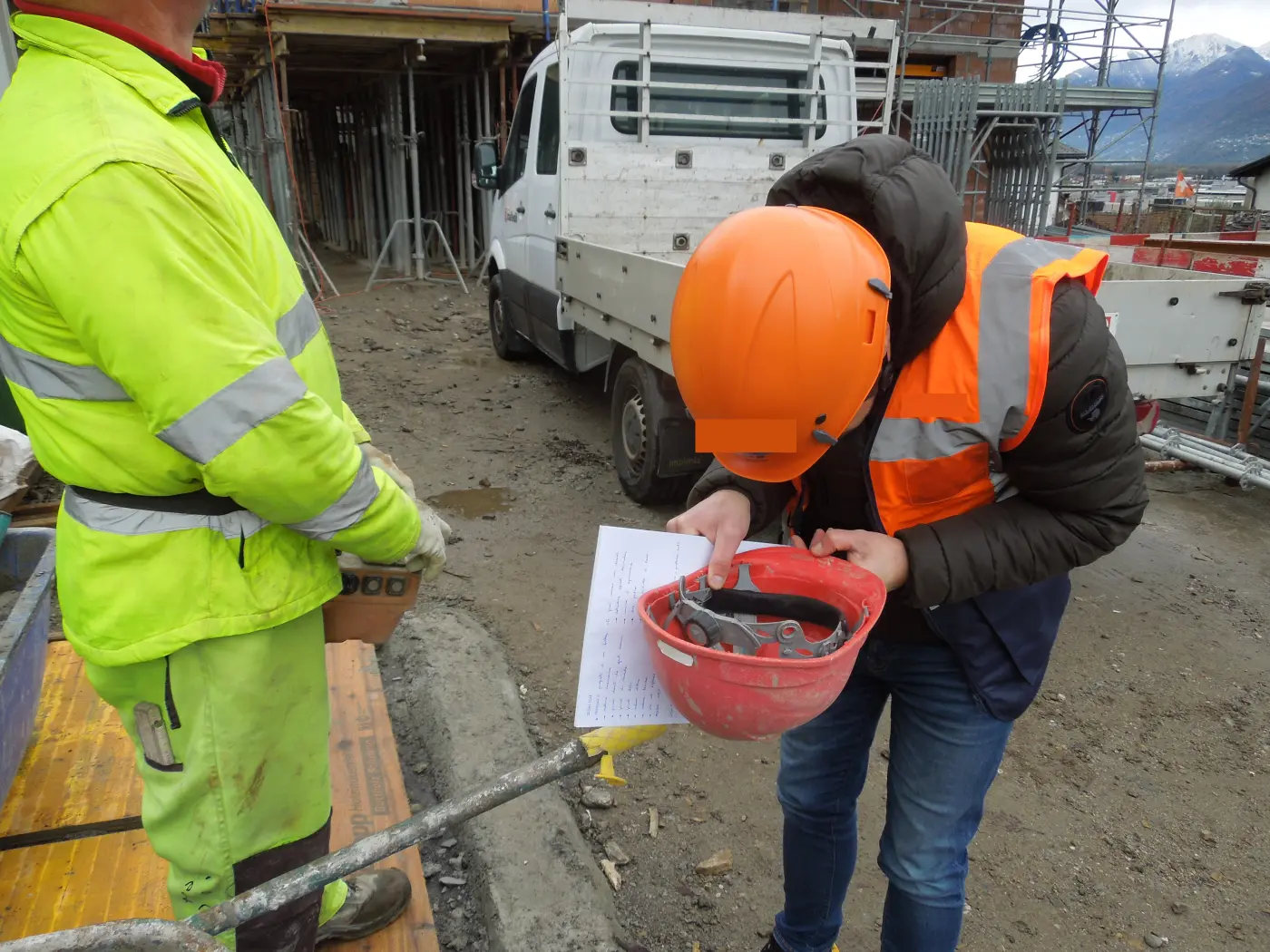 Formazione sul cantiere: un operaio con casco arancione legge una scheda di sicurezza
